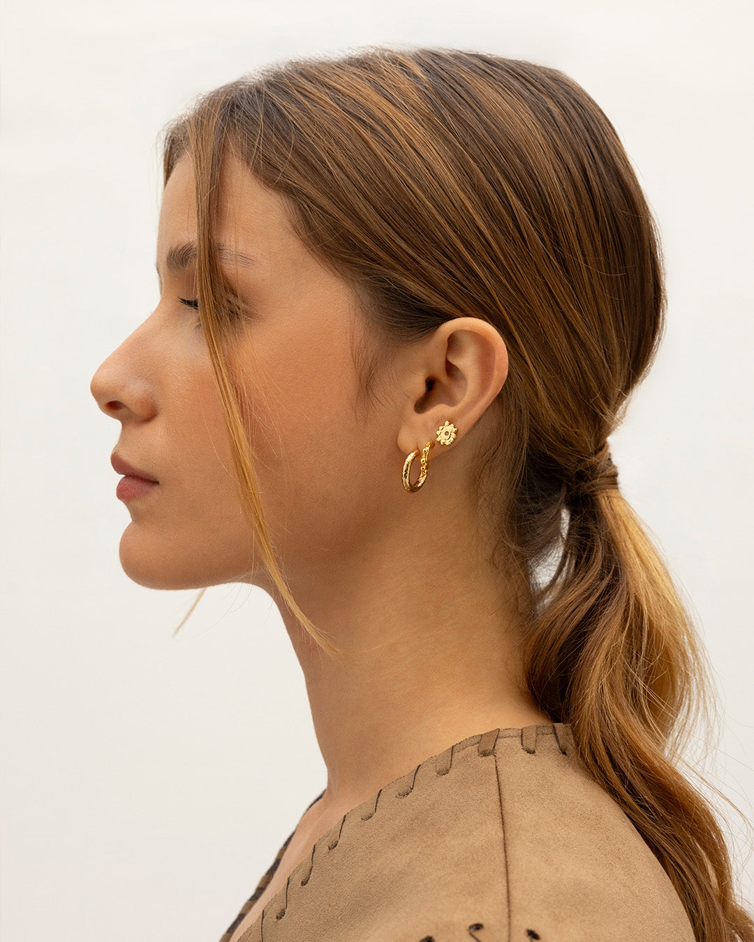 Mujer de perfil  luciendo el set de 3 Aretes Cairo que incluye topos mini sol, candongas balines y talladas