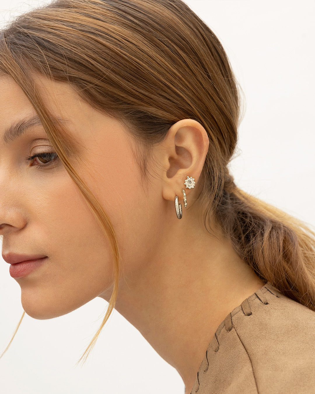 Mujer de perfil  luciendo el set de 3 Aretes Cairo que incluye topos mini sol, candongas balines y talladas