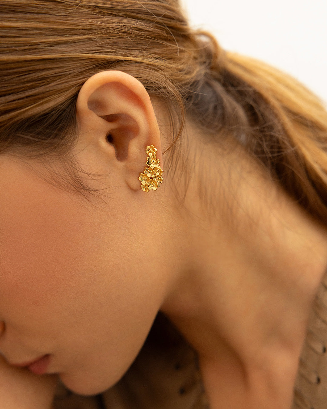 Enfoque en oreja de mujer luciendo los aretes Passionara con diseño de flores