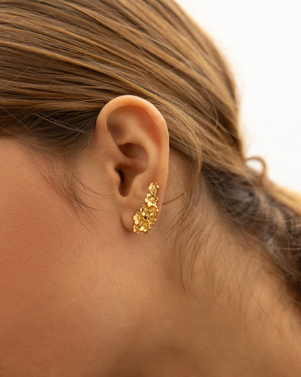 Enfoque en oreja de mujer luciendo los aretes Passionara con diseño de flores